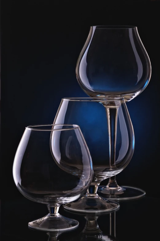 three glasses with one empty, one blue sitting in front of a black background