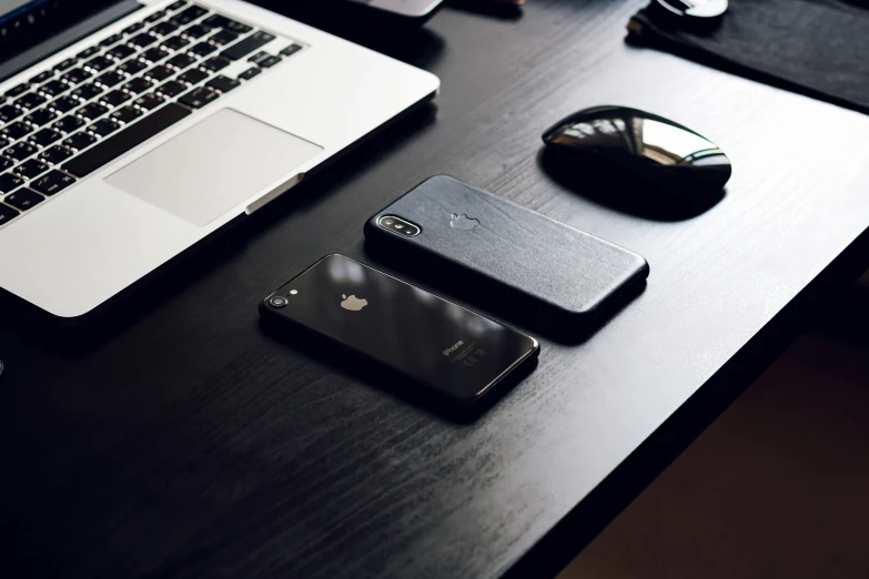 a pair of cell phones laying on a desk next to laptop