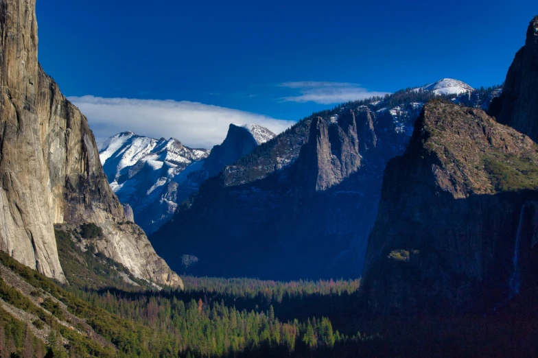 looking at a valley with trees, mountain peaks and snow capped mountains in the distance