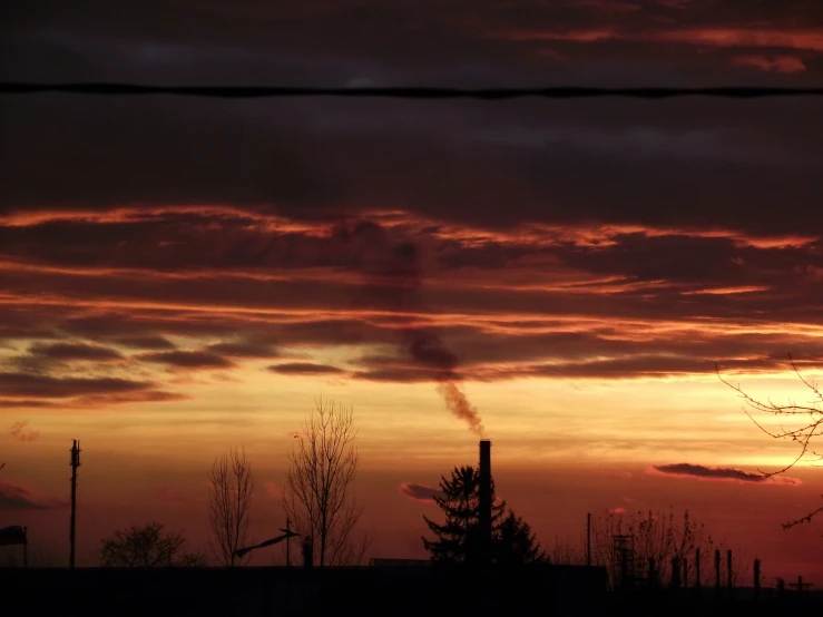 a large factory with smoke coming from it and silhouettes trees