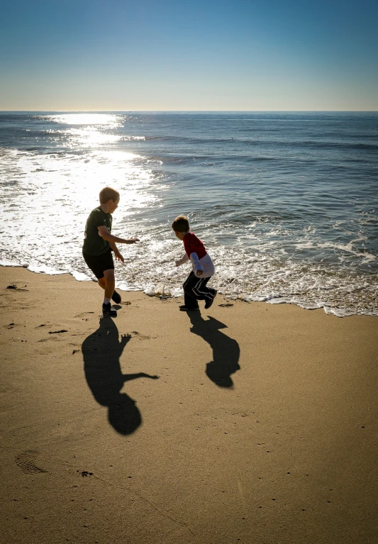 three boys running on the beach towards the ocean