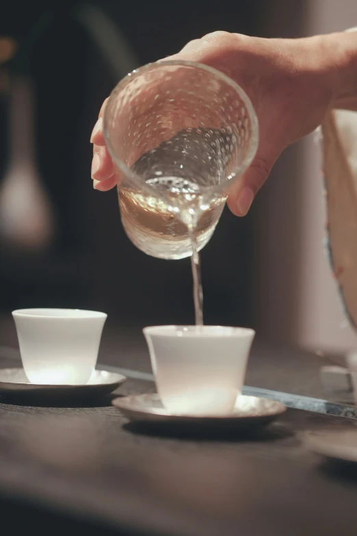 someone pouring soing into small cups on a table