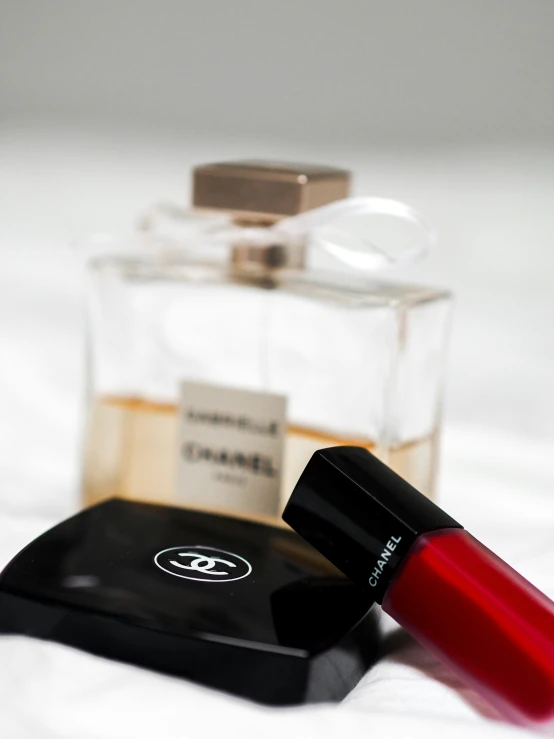 a small square bottle with a lip lacon and a red lipstick tube