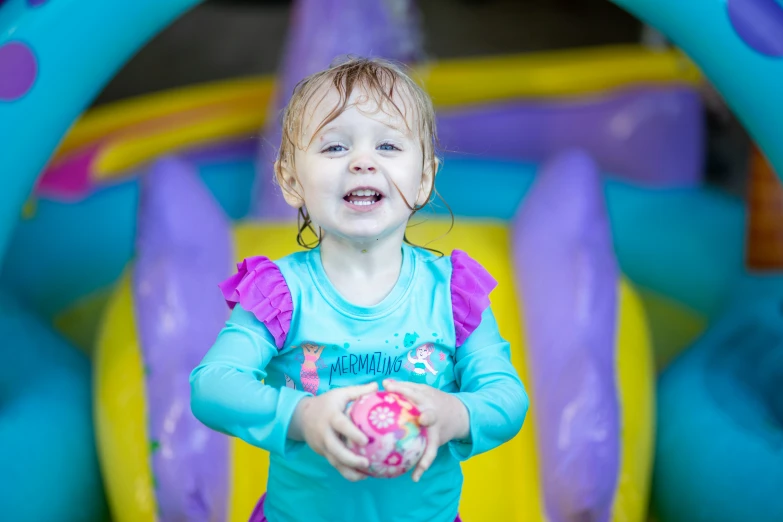 a small child in blue is smiling while holding a ball