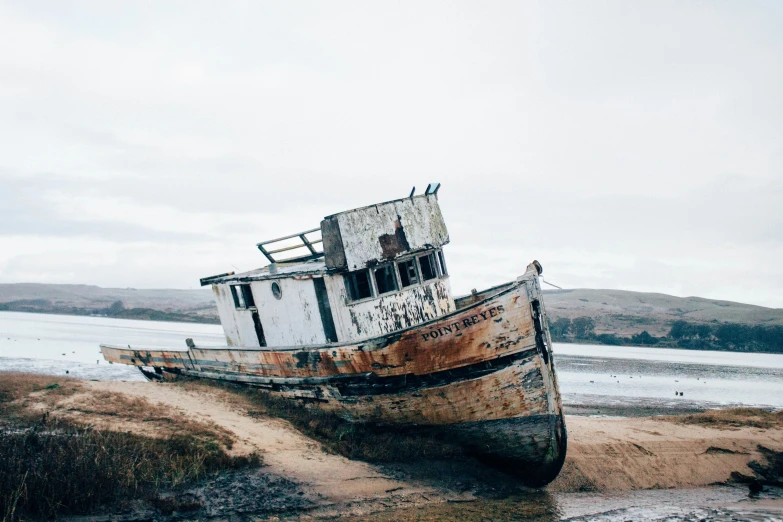 an old rusty boat sits on the sand by water