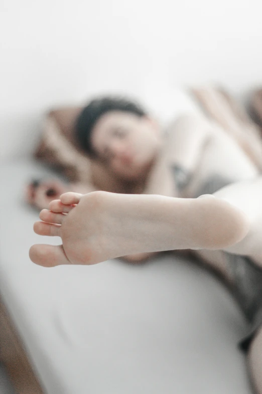 a woman laying in bed while the lady is sleeping on the floor behind her