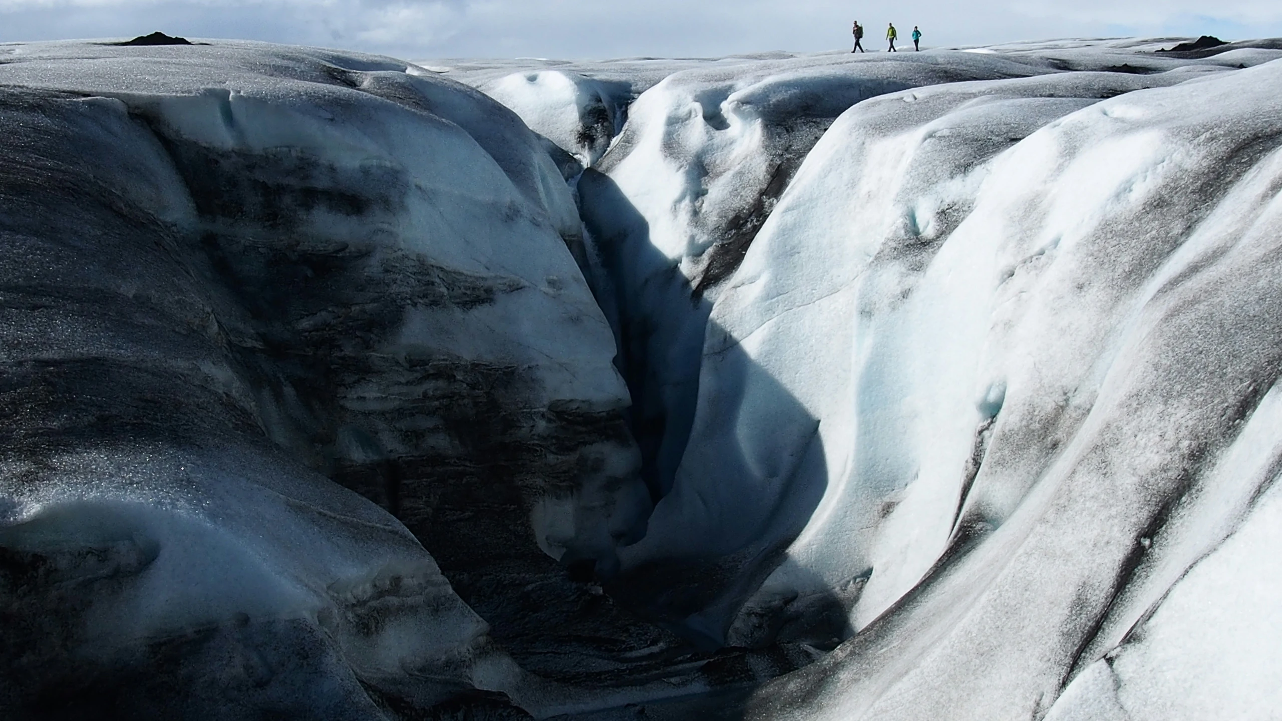 three people standing on top of a partially frozen mountain