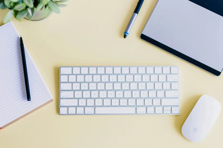 white keys are on a keyboard beside a notepad, a pen and a laptop