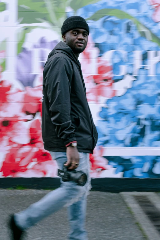 a man in grey jacket walking past colorful wall