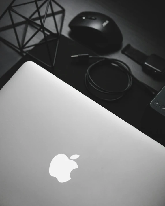 the apple laptop sits beside some other technology on the table