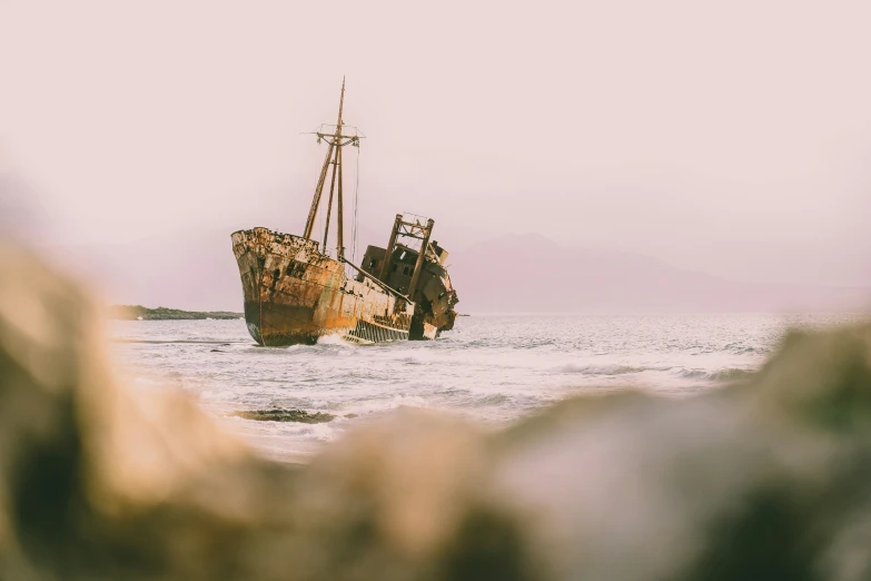 an old ship floating in the ocean next to rocks