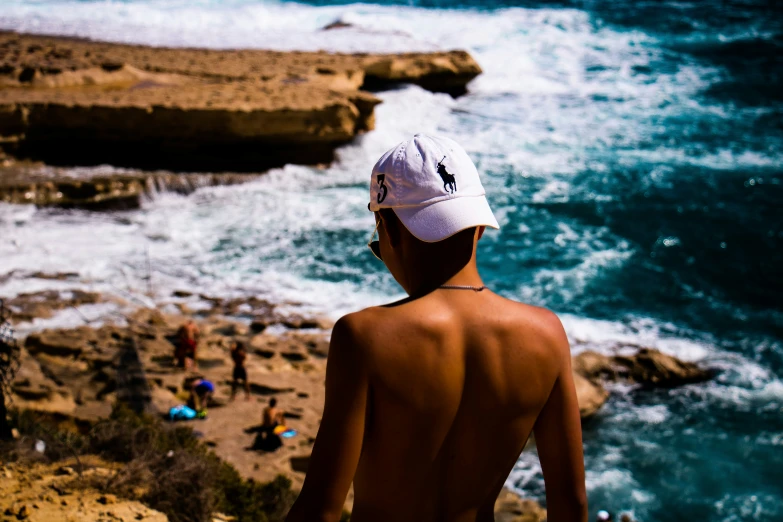 man standing on the edge of cliff looking out over beach and ocean