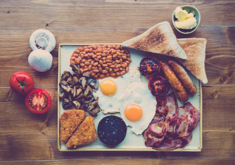 a meal on a square plate that includes eggs, bacon, toast and ham