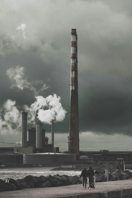 two people walking down the sidewalk towards a smoke stack