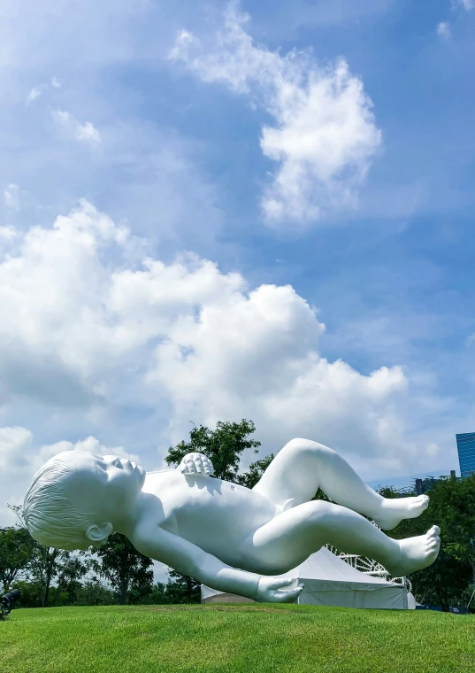 a white sculpture of a woman laying on top of a green field