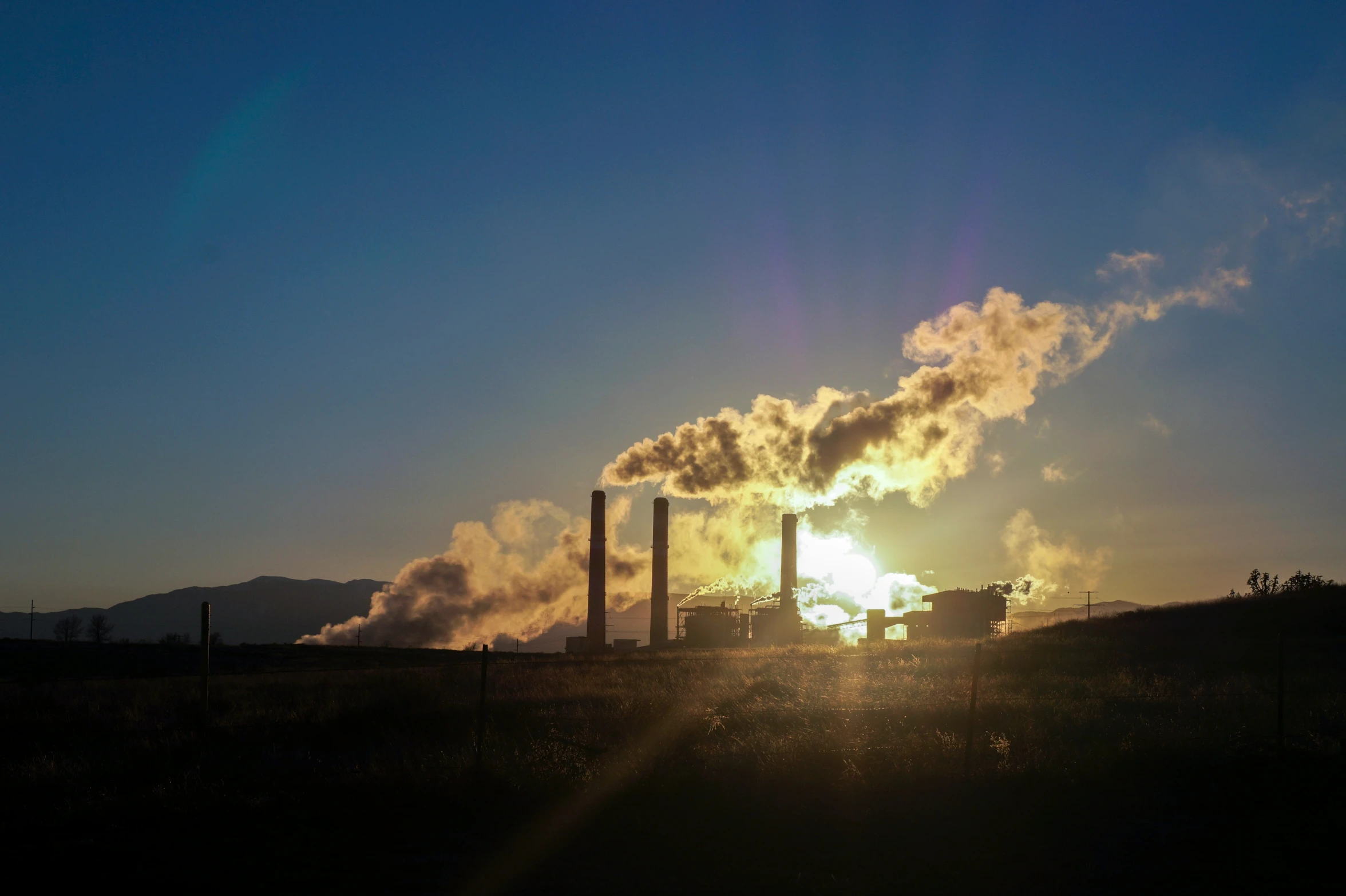 the sun is rising behind a large industrial factory