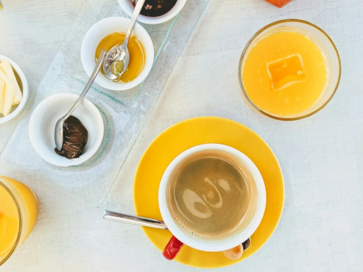 a table with three cups of coffee, two spoons, a plate of food and a bottle of orange juice