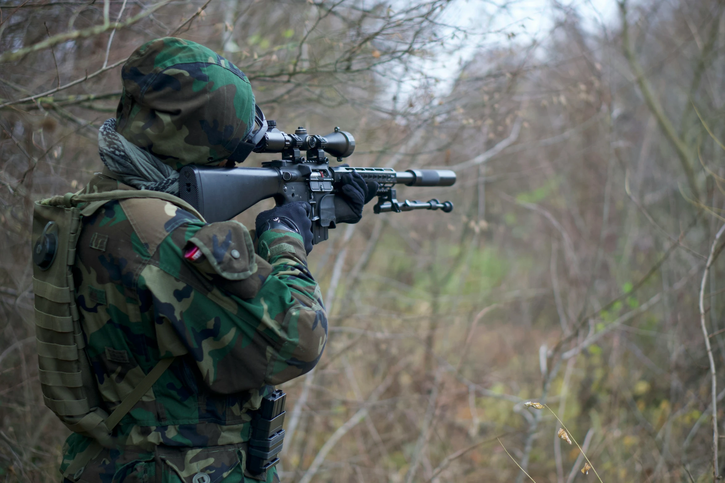 a man in camouflage holding a rifle near a wooded area