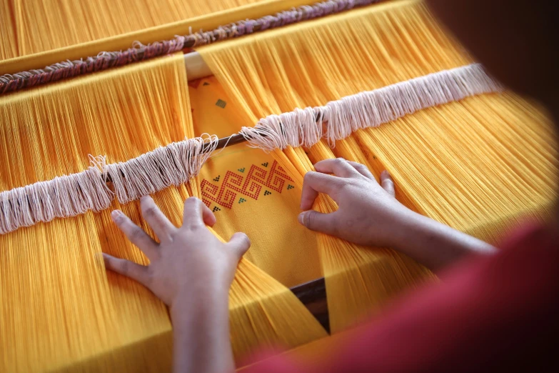 two hands are weaving fabric on a large warping machine