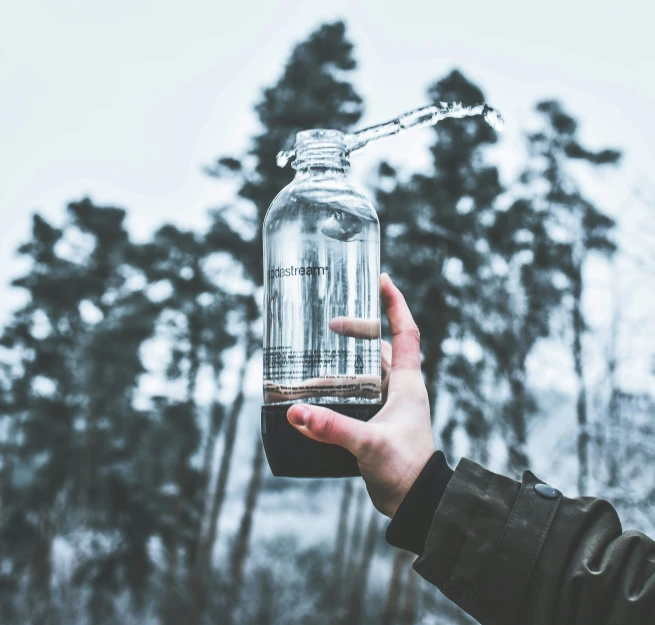 a person's hand holding a bottle with a cigarette attached to it