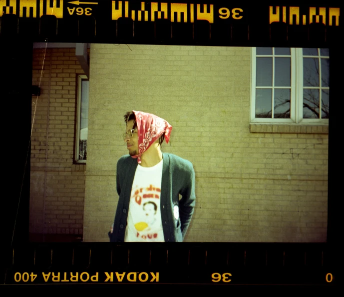 a guy with a bandana in his head stands by a brick wall