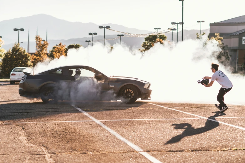 man standing next to a car in parking lot surrounded by smoke