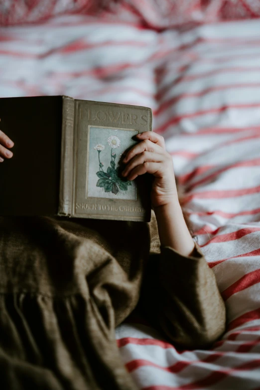 a woman laying in bed with her face up holding an open book