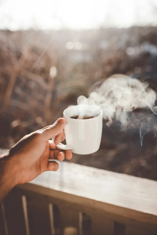 a persons hand holding a coffee cup with steam rising from it