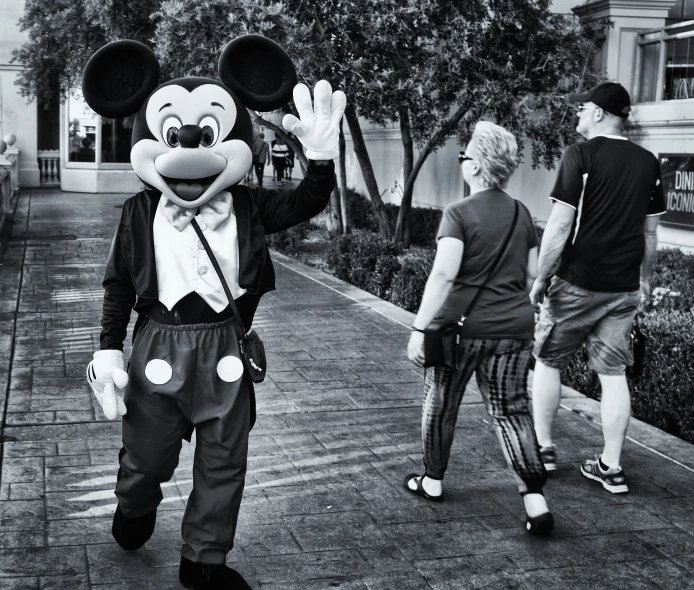 two people walk down a sidewalk with a disney character on his face