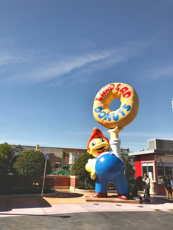 an outdoor sculpture of a man and a doughnut hangs from the pole