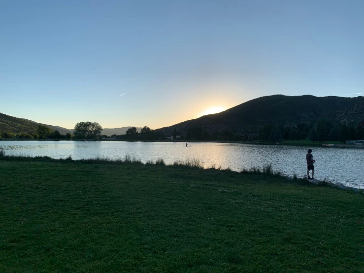 a man is standing near the water at sunset