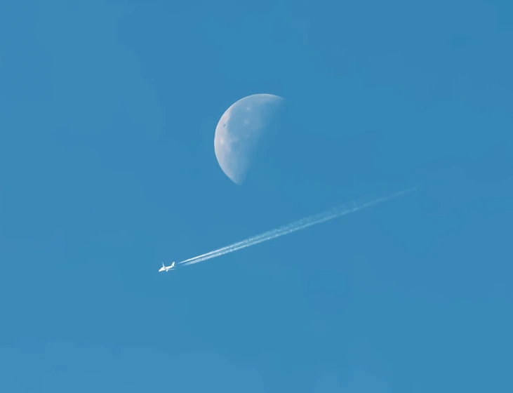 a plane flying past the moon in a blue sky