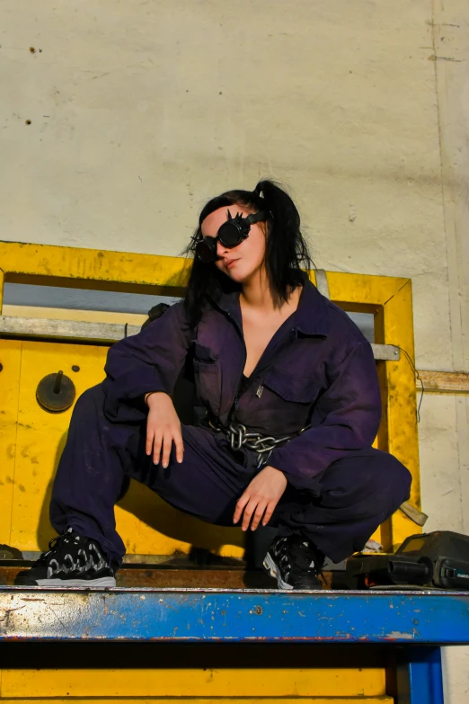 a woman wearing black sunglasses and holding on to her legs with one leg on a blue table