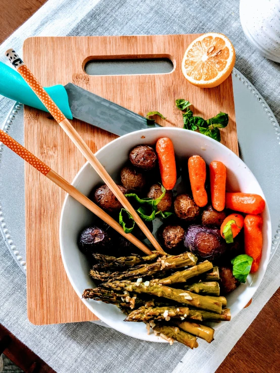 a bowl of vegetables is sitting next to chop sticks and an orange