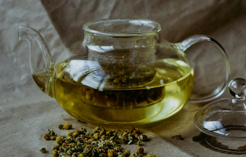 a glass teapot with a teabag next to it and a cup of green tea