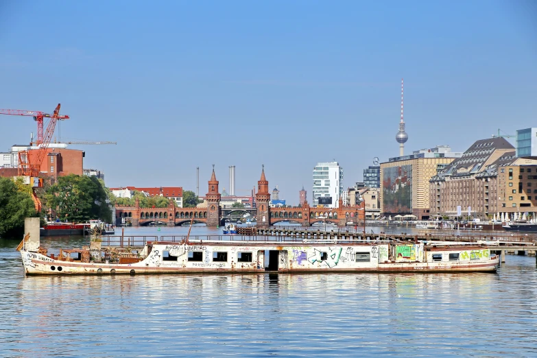 an empty ferry is seen in the foreground with buildings, cranes and water