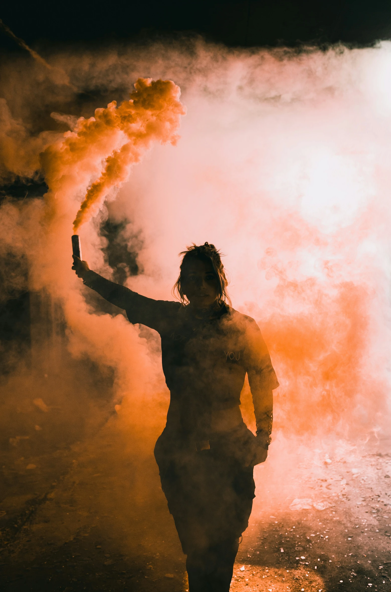 a woman holds her arm up as she stands in front of a small fire