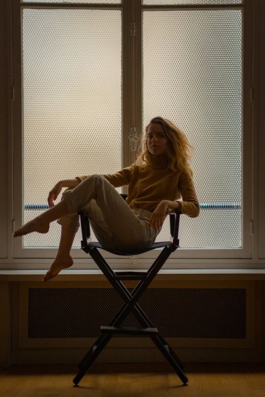 a woman sitting on a director's chair in front of a window