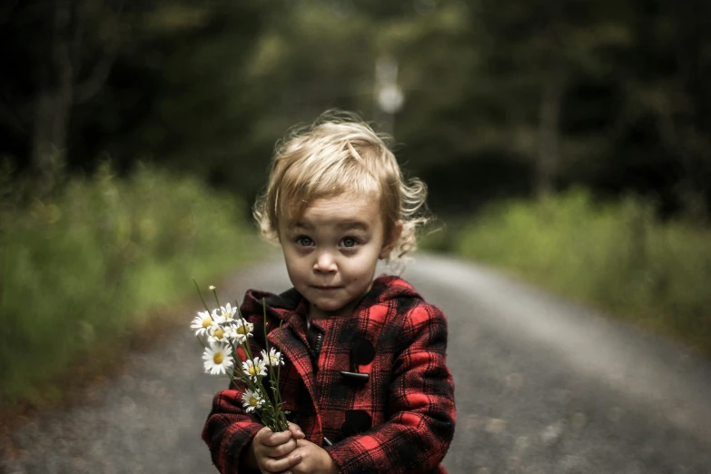 little girl holding flowers in front of a country road