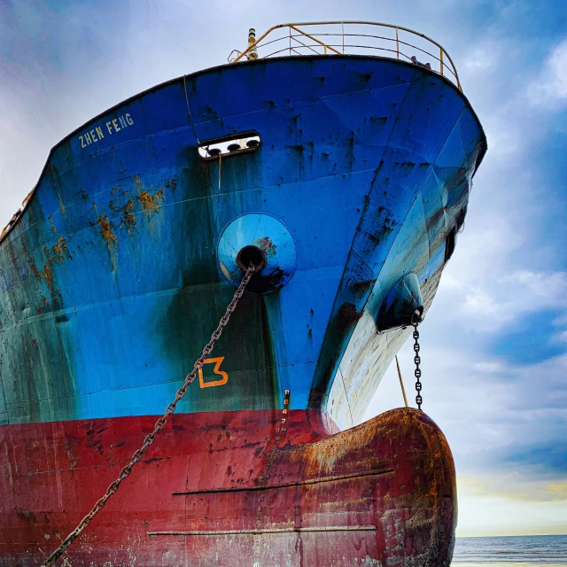 an old rusted and blue ship is docked on the sand