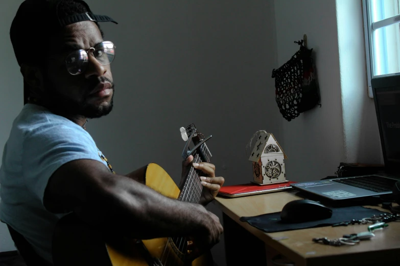 man with glasses plays a guitar at his desk