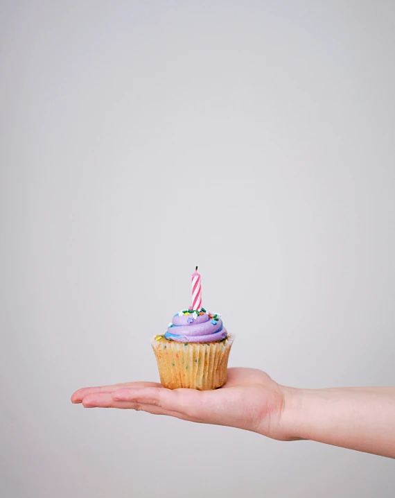 a hand holding a small cupcake with two candles on top