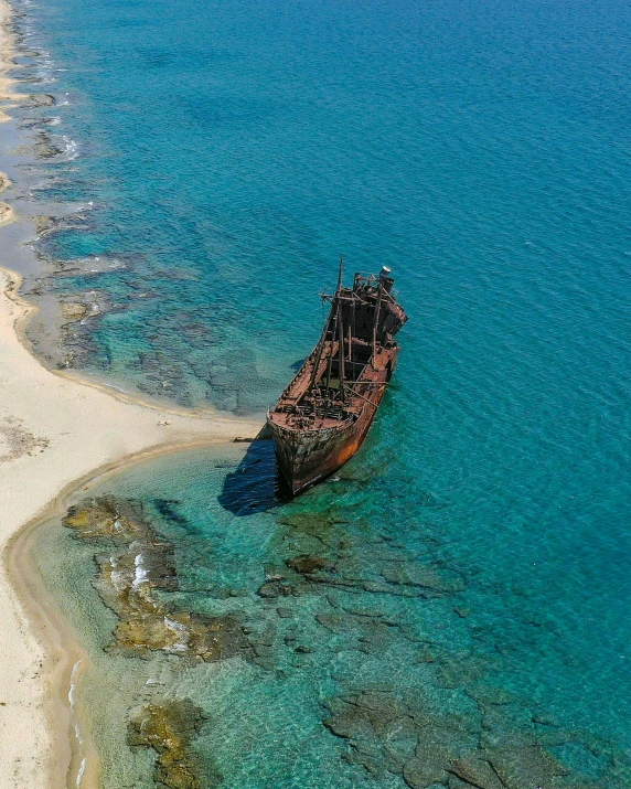 an old boat lies on the beach beside a beach with blue water and some corals