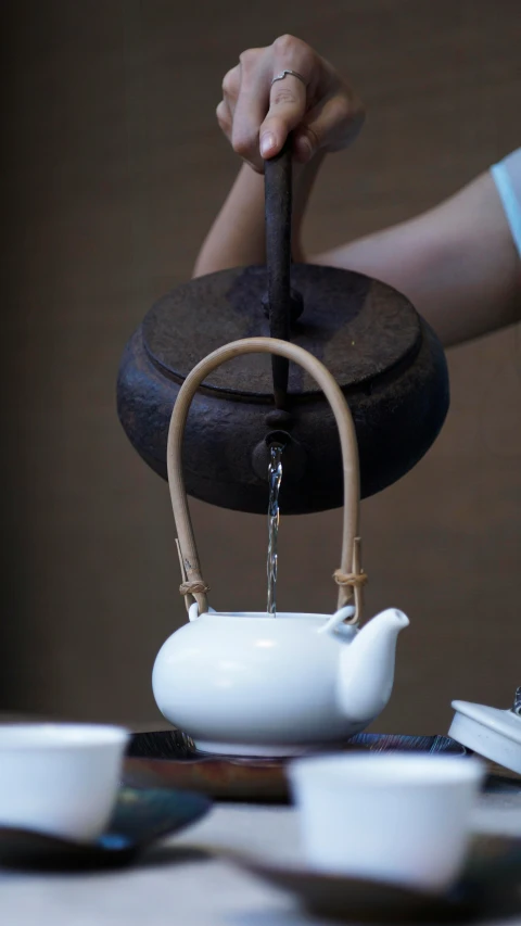 a person pours a tea kettle into a white teapot