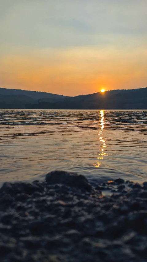 the sun setting over a calm lake with mountains in the background