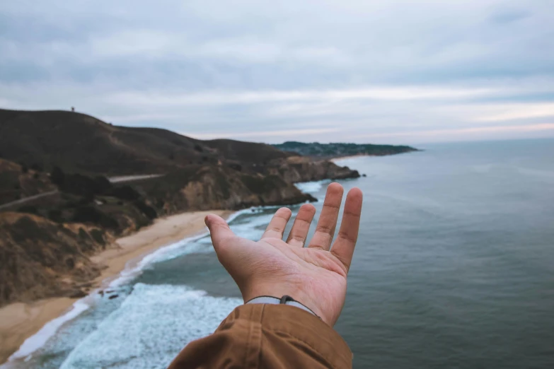 person's hand reaching out to the ocean with a view from atop