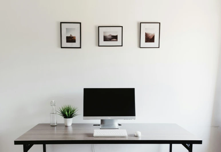 the desk has a computer, cell phone, and potted plant on it