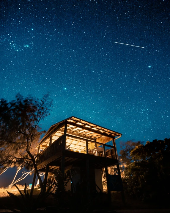 a night view of the stars, above a house with a porch and wraparound balcony