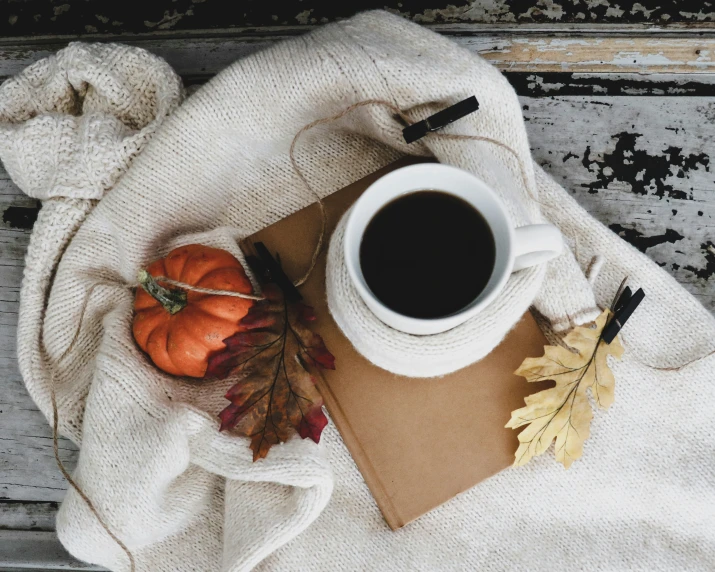 a white cup of coffee next to some oranges and an orange leaf