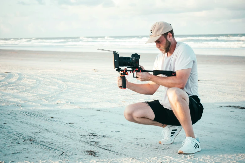 man kneeling down on the beach holding up a small object